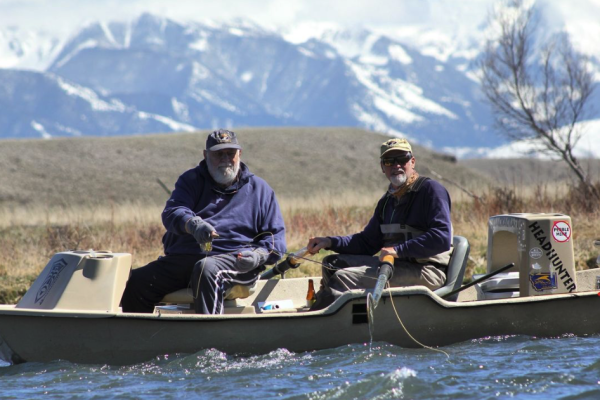two men in drift boat fishing in montana with snowcapped mountains in the background
